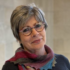 woman smiling with glasses short blonde hair and a multicolored scarf