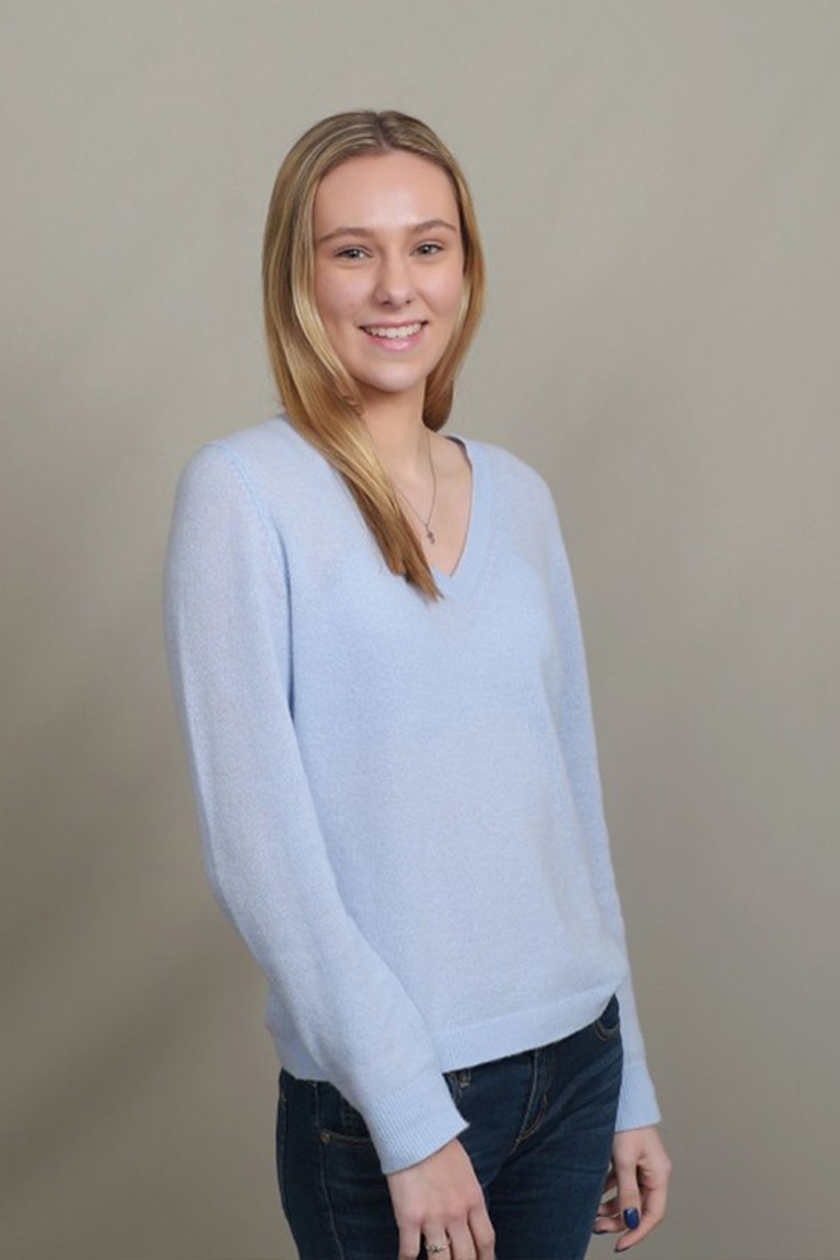 A woman with blonde hair wearing a light purple sweater and black pants