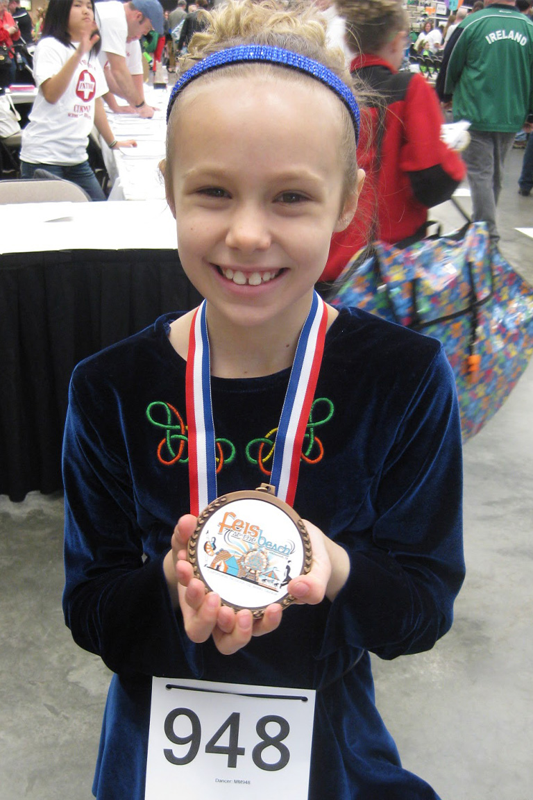 Girl with blue velvet irish dress on, holding a medal