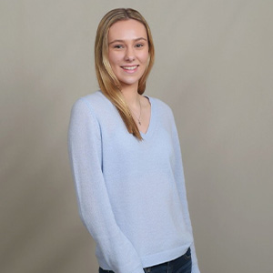 A woman with blonde hair wearing a light purple sweater and black pants