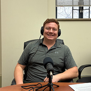 man in short sleeved polo sitting in front of microphone with headphones on.