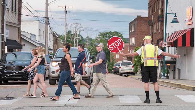 crossing guard with neon vest holding stop sign while pedestrians cross street