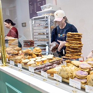 two women working at a coffee shop holding cookies behind the counter