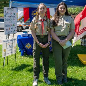 two young girls in scout uniforms stand near table with scout information