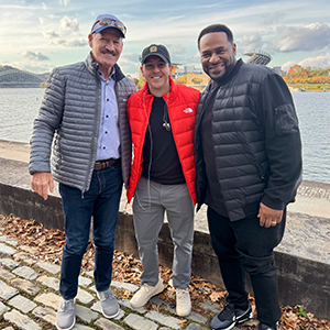three men smiling in front of river and football stadium in pittsburgh