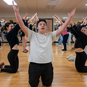 teenagers kneeling with arms above their heads practicing for a musical