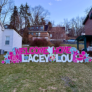 front yard with a large sign display that reads welcome home lacey lou in pink and white
