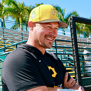 man in yellow pirates baseball hat smiling with palm trees in background