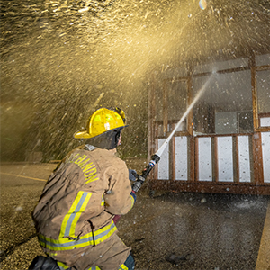 firefighter spraying firehose at structure