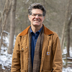 man in brown coat smiles outside in a park with snow