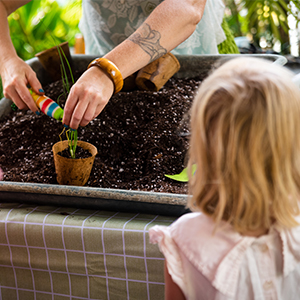 hands potting a plant in a small brown pot and a child watching