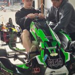 Teen in green kart with man next to him working on the kart.