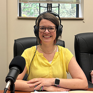 woman in yellow short sleeved top behind microphone wearing headphones