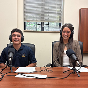 a teen boy sits to the right of a teen girl. both are wearing headphones and sitting in front of a microphone.